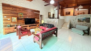 A spacious living area with a wooden entertainment unit, a large flat-screen TV, a sofa, and a stone wall.