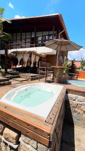 A hot tub in a wooden frame with a pool in the background. - EcoHotel Vale do Sol (Embu das Artes)