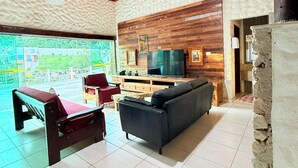 A spacious living area with a wooden ceiling, a large flat-screen TV, a sofa, and a red lounge chair.