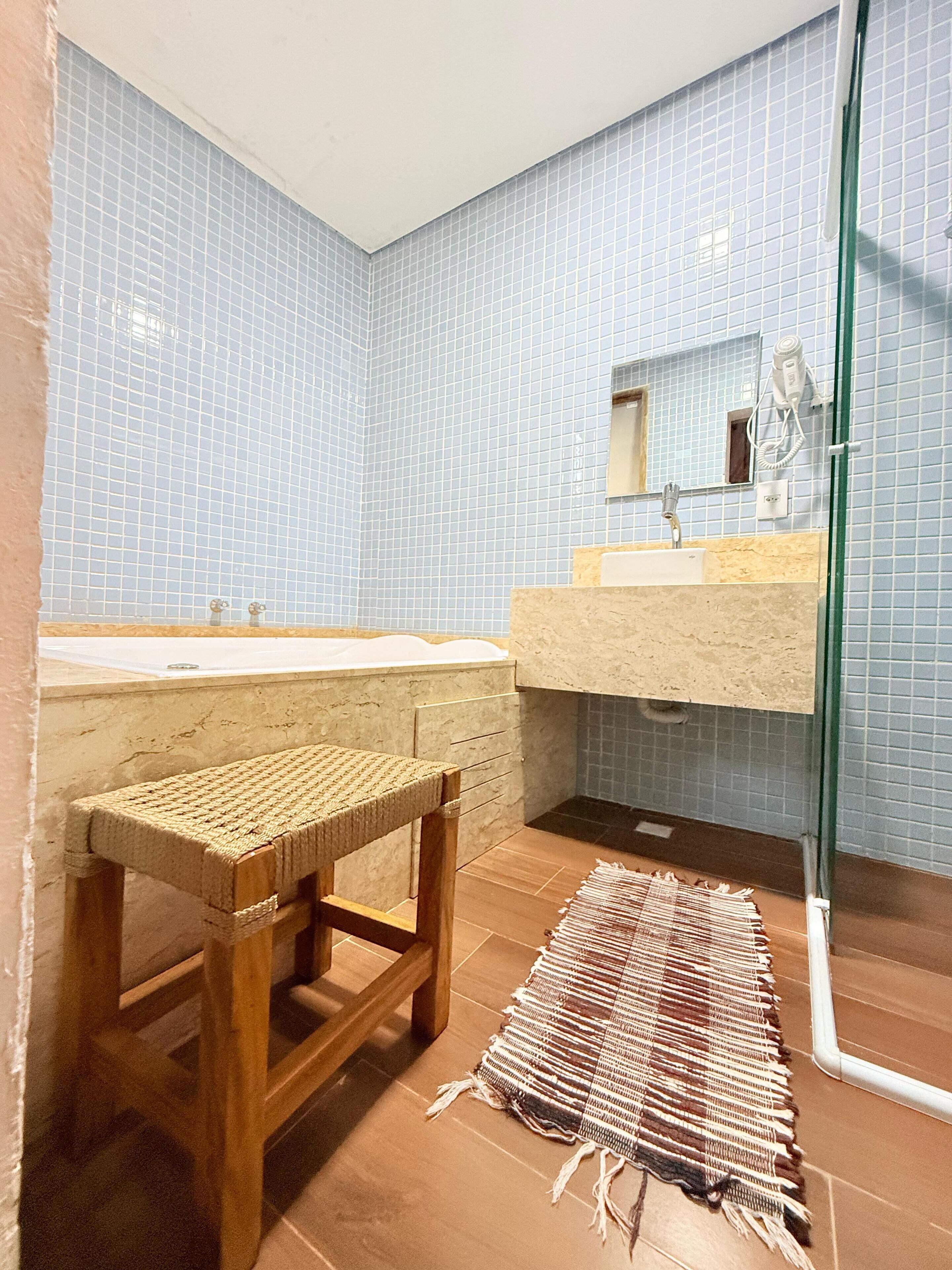 A bathroom with a wooden stool, a sink, and a glass shower enclosure.
