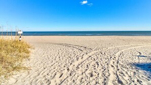 A sandy beach with footprints leading to the water, a clear sky, and a signboard in the background.