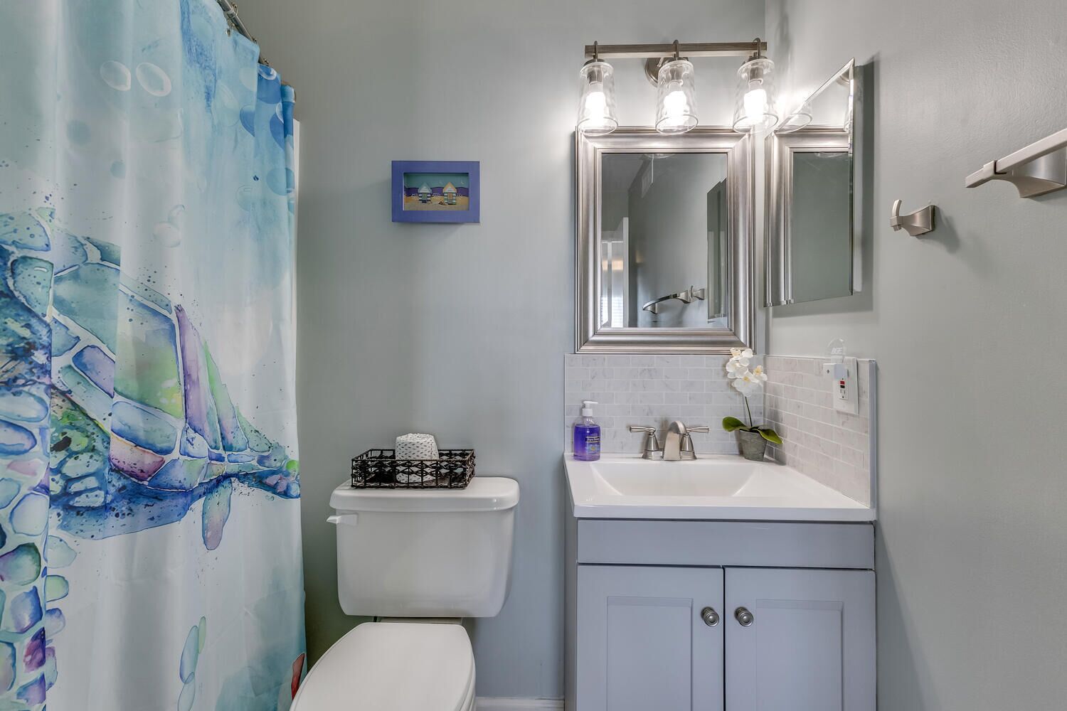Un baño con inodoro, lavamanos con espejo y cortina de ducha con diseño abstracto azul y verde.