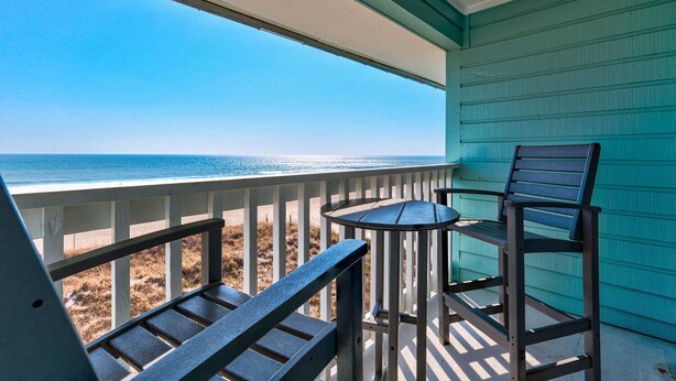 A balcony with a view of the ocean, a table, and two chairs.