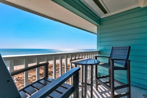 A balcony with a view of the ocean, a table, and two chairs.