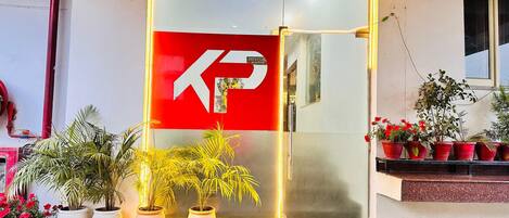 A reception area with a red and white sign, potted plants, and a staircase.