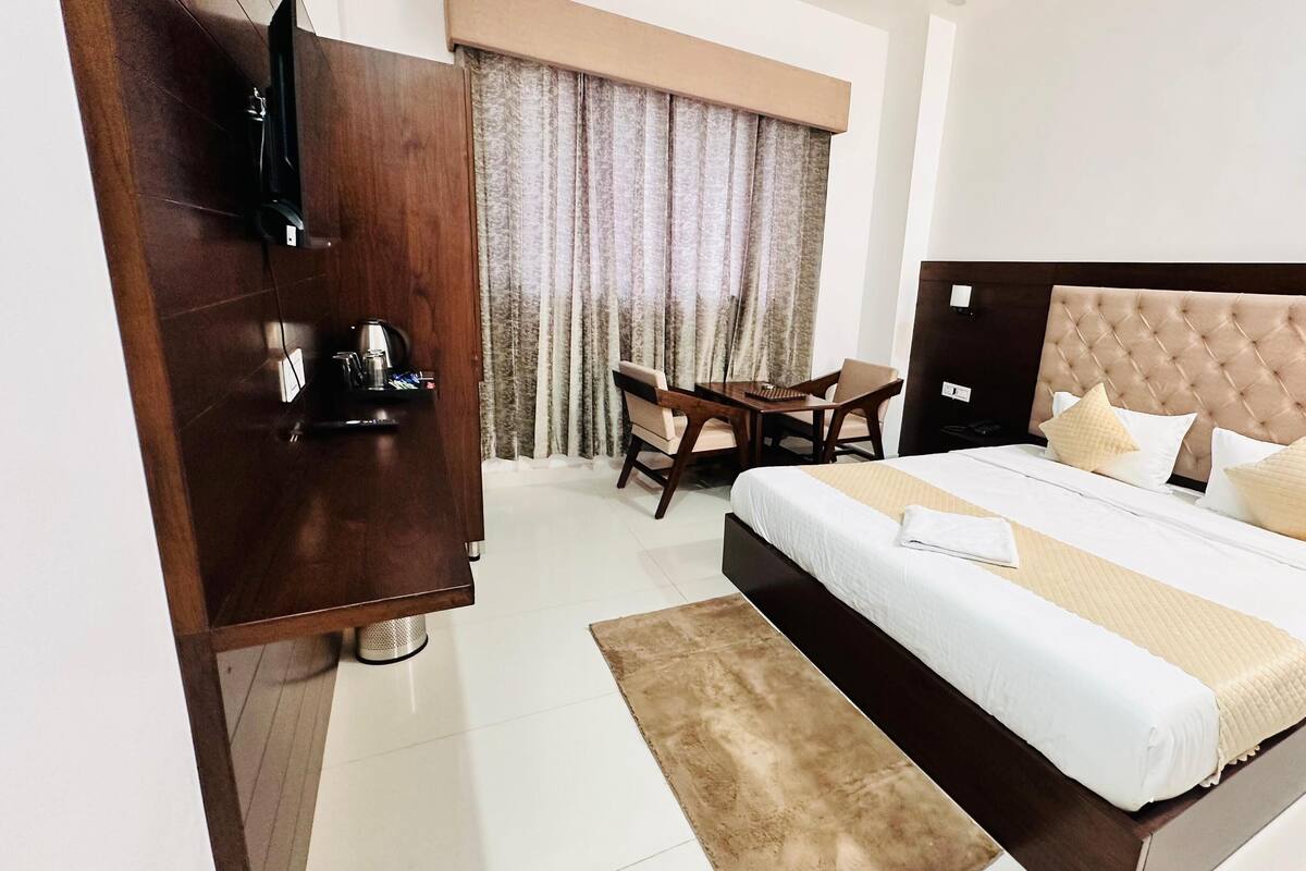 Habitación de hotel con una cama grande, una mesita de noche de madera, un escritorio con dos sillas y una ventana con cortinas.