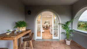 Uma área de refeições acolhedora com uma mesa e cadeiras de madeira, uma planta em vaso e vista da sala de jantar por uma porta arqueada.