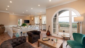Uma sala de estar ampla com espaço para refeições, lareira e vista através de uma porta em arco.
