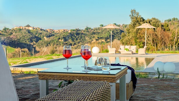 Mesa com duas taças de vinho e um caderno, com vista para uma piscina e uma encosta panorâmica.
