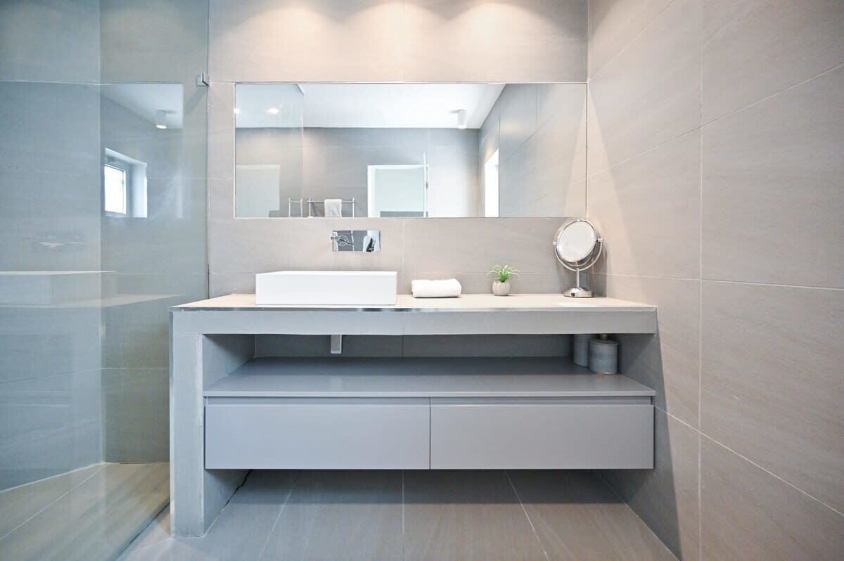 Une salle de bain moderne avec un grand miroir, un lavabo blanc et une petite plante en pot.