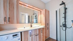 Un bagno moderno con mobili in legno, una lavatrice integrata, uno spazio doccia in vetro e un grande specchio.