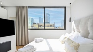 A modern hotel room with a large bed, a flat-screen TV, and a city view through a large window.