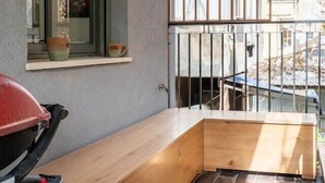 Een balkon met een houten bankje, een raam met decoratieve objecten en een uitzicht over de stad.
