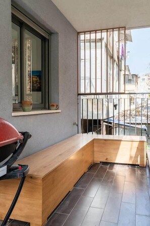 Een balkon met een houten bankje, een raam met decoratieve objecten en een uitzicht over de stad.