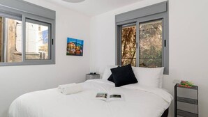 Een slaapkamer met een groot bed, twee nachtkastjes en een raam met uitzicht op bomen.
