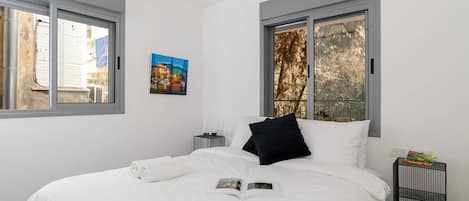 A bedroom with a large bed, two bedside tables, and a window with a view of trees.