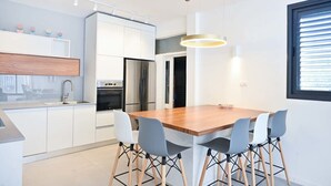 Une cuisine moderne avec des meubles blancs, des appareils en acier inoxydable et une table à manger en bois, accompagnée de quatre chaises.