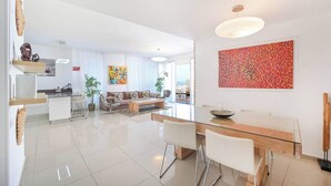 Un salon moderne avec une table à manger en verre, des canapés blancs et un grand tableau abstrait.