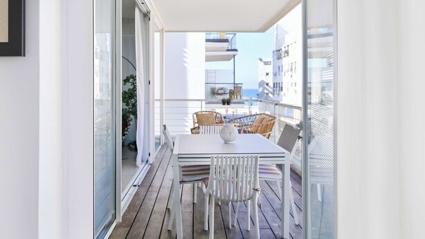 Un balcon avec une table et des chaises, une porte vitrée et une vue sur des immeubles et une étendue d’eau.