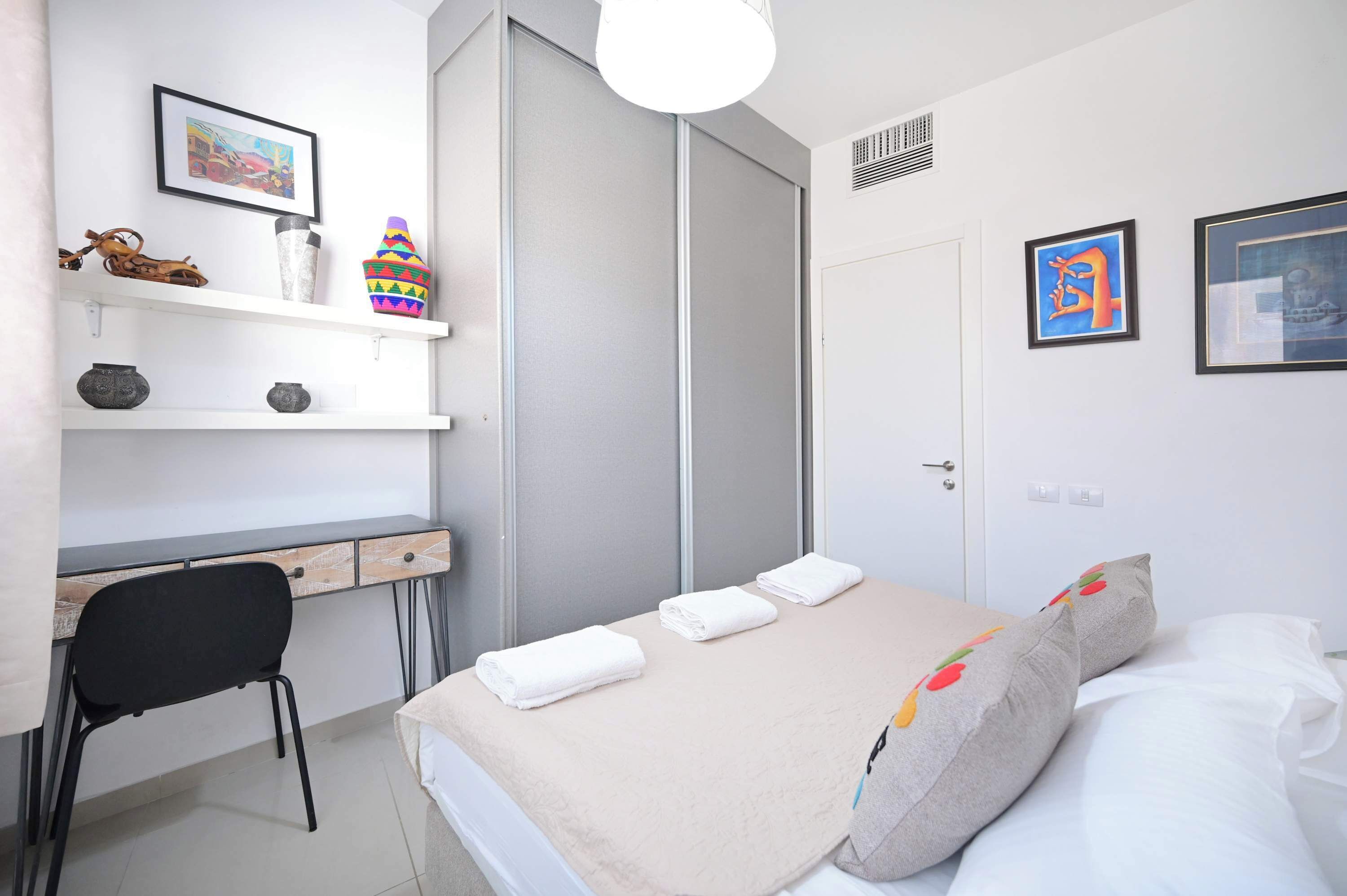 Een moderne slaapkamer met een bed, bureau, stoel en een kledingkast.