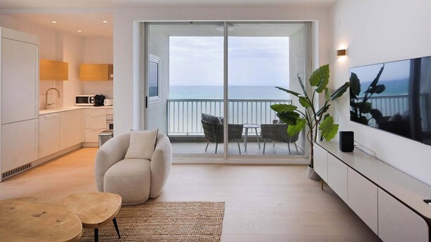 Een moderne woonkamer met een bank, een televisie en een balkon met uitzicht op zee.
