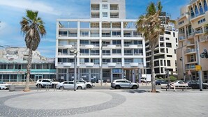 Een modern meerlaags gebouw met balkons, een parkeerplaats en palmbomen.