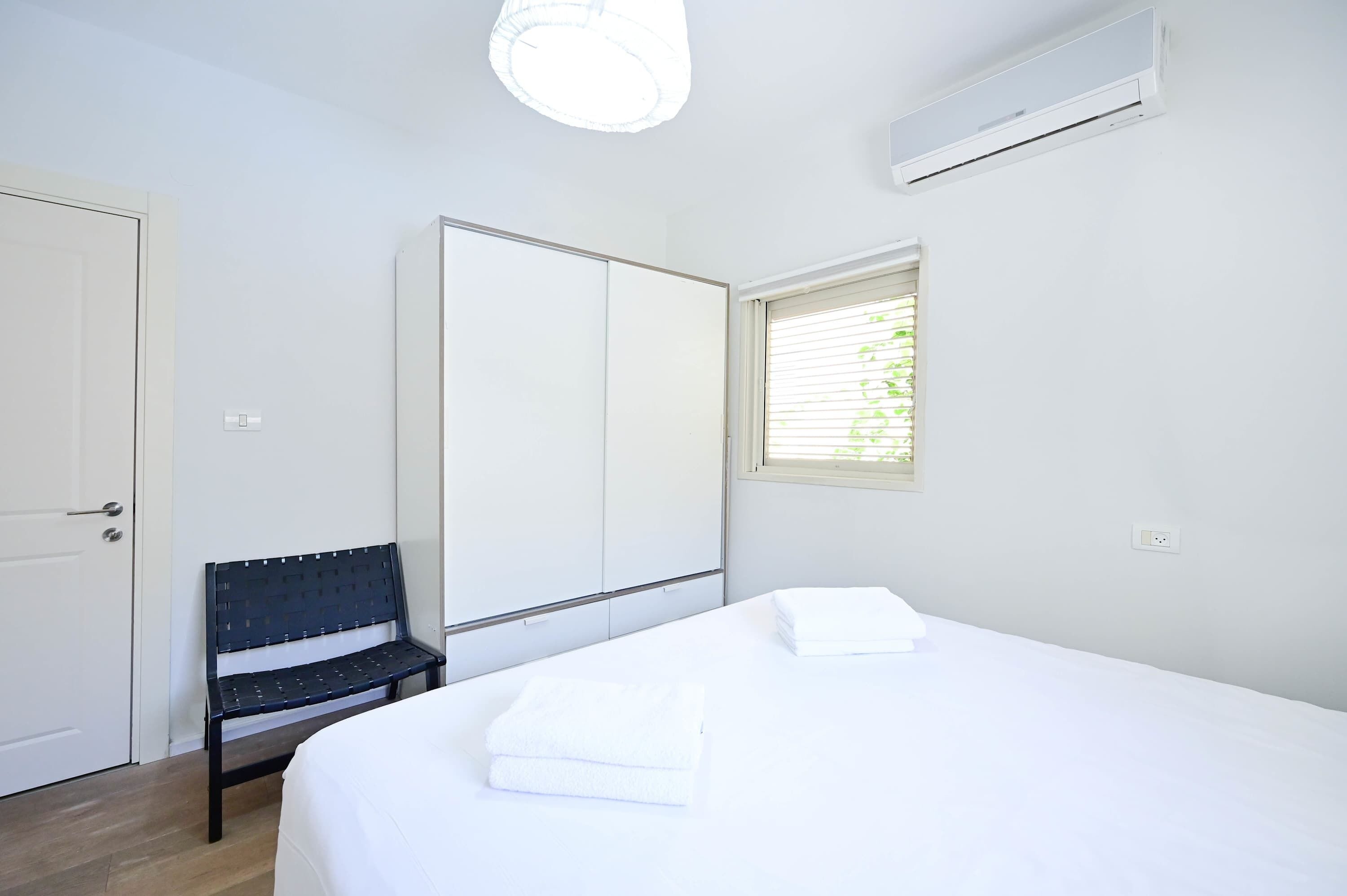 A bedroom with a bed, a bench, a wardrobe, and a window with blinds.