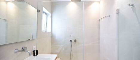 A modern bathroom with a glass-enclosed shower, a large mirror, and a white sink.