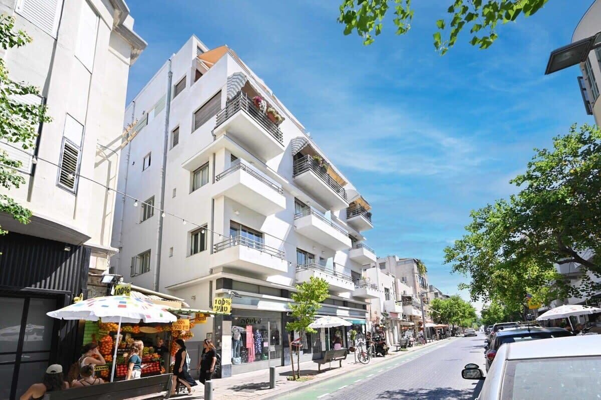 Eine Straße mit modernen Gebäuden, Außenplätzen und einem Obststand.