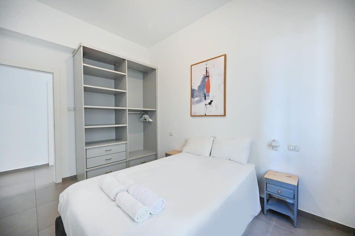 A hotel room with a bed, a wardrobe, a bedside table, and a painting on the wall.