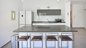 Une cuisine moderne dotée d’un îlot central, de tabourets de bar, d’appareils électroménagers en acier inoxydable et de luminaires suspendus.