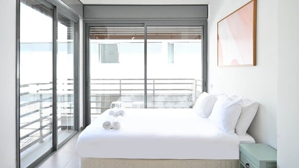 Une chambre d’hôtel moderne avec un grand lit, un balcon doté d’une balustrade et un tableau encadré au mur.