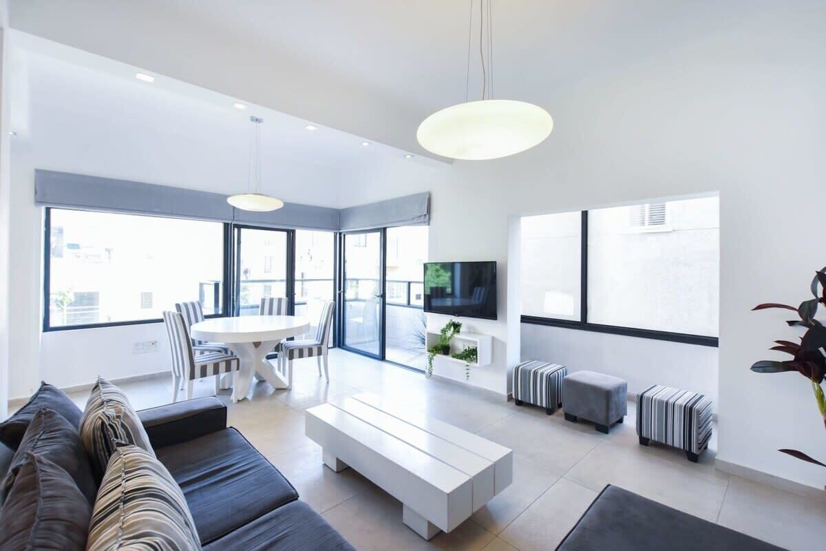 A modern living room with a sofa, a coffee table, a TV, and a dining area with chairs and a table.