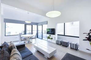 A modern living room with a sofa, a coffee table, a TV, and a dining area with chairs and a table. - Zebra's Stripe by HolyGuest (Tel Aviv)