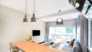 A modern kitchen with a wooden countertop, hanging pendant lights, and a flat-screen TV mounted on the wall.