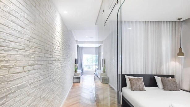 A modern hotel room with a brick wall, a large bed with white linens, and a glass partition.