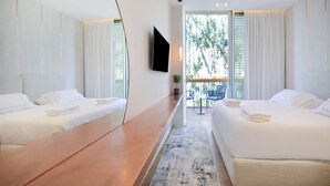Une chambre d’hôtel moderne avec deux lits, un grand miroir, un téléviseur à écran plat et un balcon offrant une vue sur les arbres.