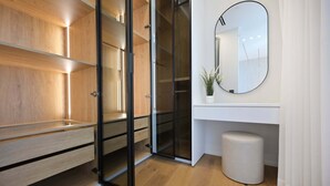 Une chambre moderne avec une armoire en bois, un placard à porte en verre, un miroir rond et un petit tabouret blanc.