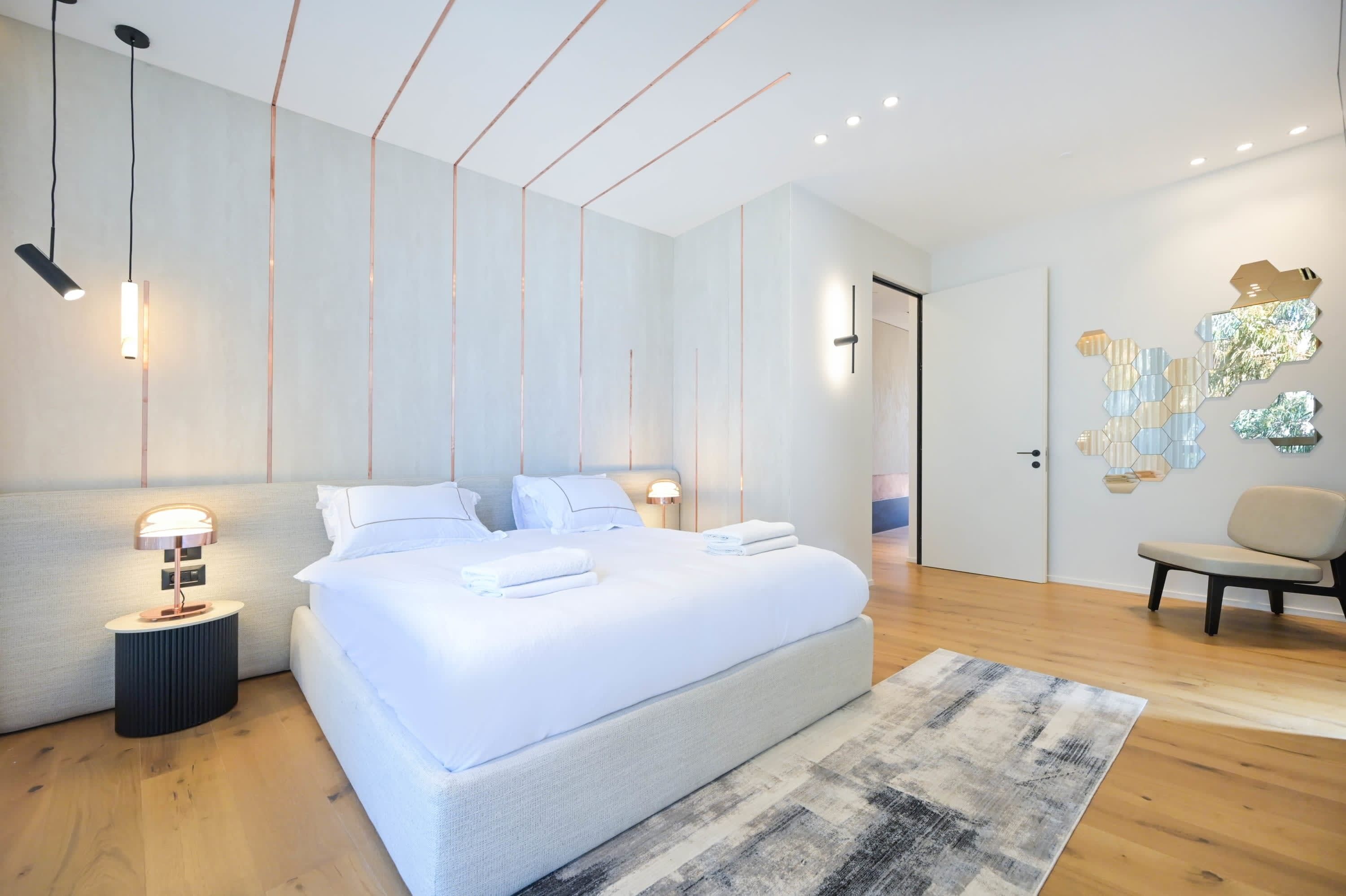 A modern bedroom with a large bed, bedside lamps, a wooden floor, and a decorative wall piece.