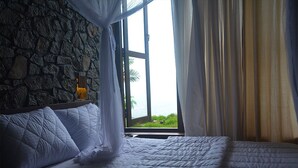 A bed with a quilted cover, a stone wall, and a window with curtains.
