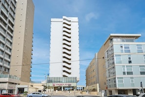 Ein modernes Hotel mit einem zentralen Turm, mehreren Balkonen und blauem Himmel.
