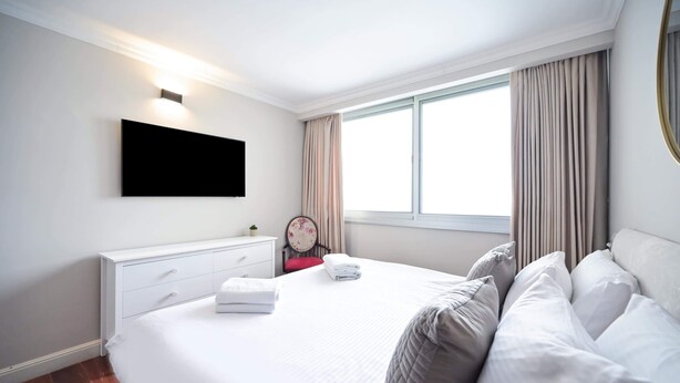 Habitación de hotel con una cama grande, un televisor de pantalla plana montado en la pared, una ventana con cortinas y una mesita de noche con lámpara.