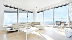 A modern living room with a large sectional sofa, a glass coffee table, and large floor-to-ceiling windows offering a city view.