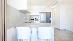 A modern kitchen with white cabinetry, a central island with bar stools, and a stainless steel refrigerator. - Cozy 1BR Apartment in Mendele by HolyGuest (Tel Aviv)