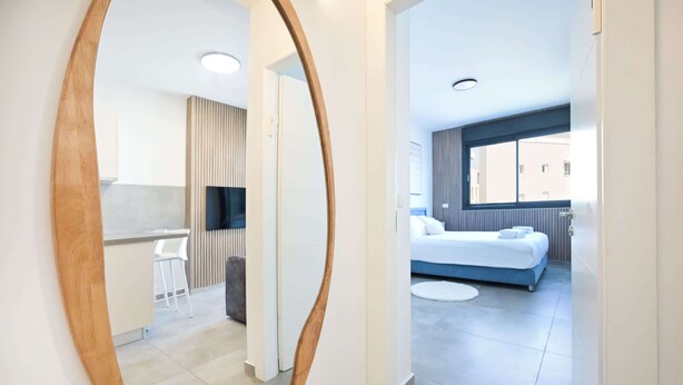 A modern hotel room with a large bed, a small desk, and a kitchenette. - Cozy 1BR Apartment in Mendele by HolyGuest (Tel Aviv)