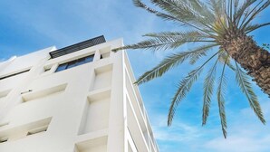 A white building with a modern architectural design, featuring a series of balconies and a central air conditioning unit. - Cozy 1BR Apartment in Mendele by HolyGuest (Tel Aviv)