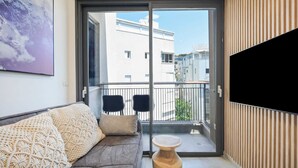 A modern living room with a sofa, a coffee table, and a balcony with a view of neighboring buildings. - Cozy 1BR Apartment in Mendele by HolyGuest (Tel Aviv)