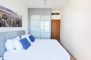 Une chambre d’hôtel moderne avec un grand lit, un tableau représentant un paysage urbain, une porte coulissante et une porte en bois.