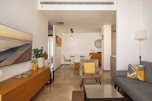 A modern living room with a flat-screen TV, a sofa, a coffee table, and a dining area with chairs and a table.