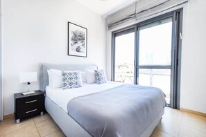 A modern bedroom with a large bed, a nightstand, a framed picture on the wall, and a large window. - Splendor 2-BR  in Melchet  by HolyGuest (Tel Aviv)